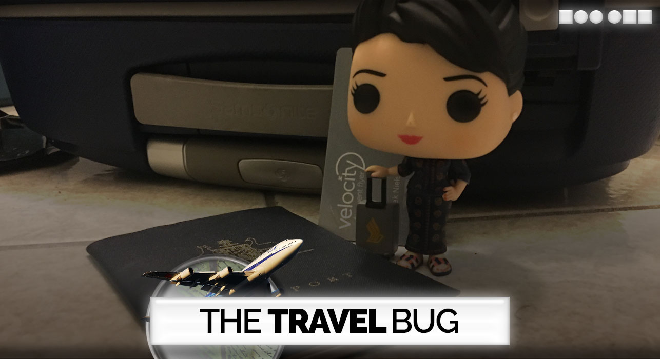 A Funko Pop Vinyl figurine of the "Singapore Girl" (Singapore Airlines' cabin crew in uniform), carrying her roll-aboard suitcase, standing next to my (old) passport.