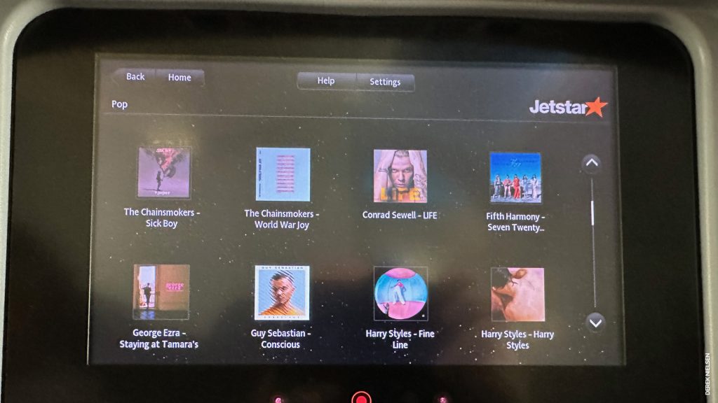The in-flight entertainment screens on a Jetstar 787 economy class seat, showing some of the albums available in the music section.