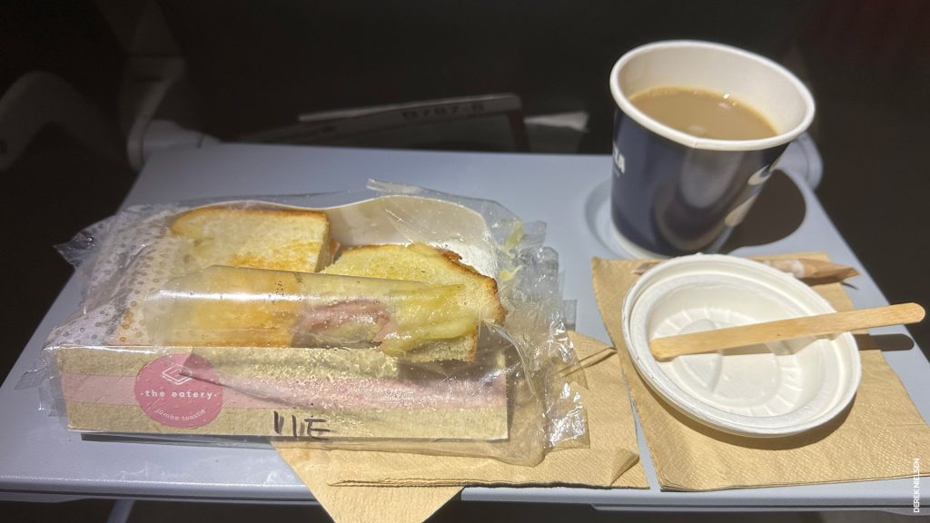 An in-flight ham and cheese toasted sandwich, with a cup of coffee.