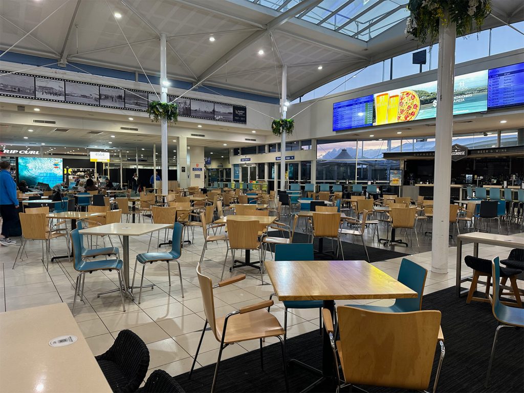 Sunshine Coast Airport's departures hall. The departures board, along with a bar serving drinks (well, not at 6am, when this photo was taken) are visible. Seats and tables are available.