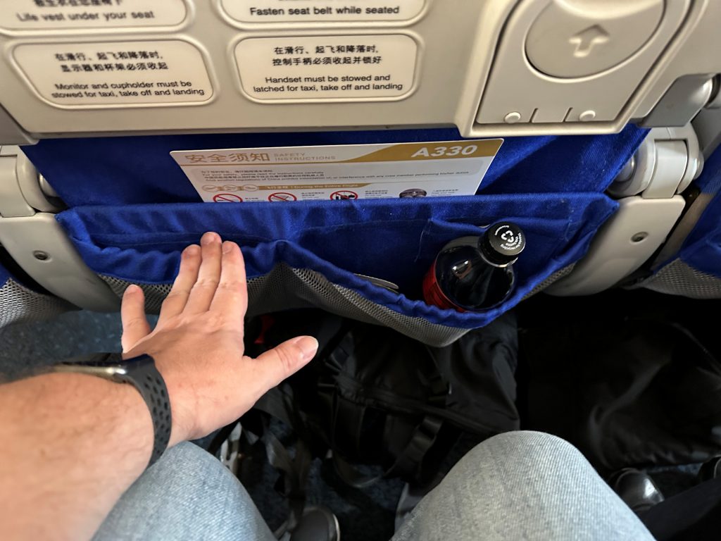 Derek shows the amount of legroom at his seat by stretching his hand from his knees.